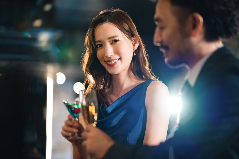 グラスを手に微笑む女性と、隣で語らう男性